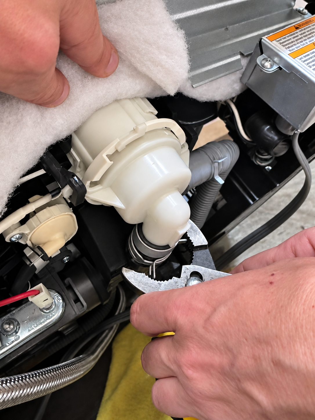 Technician removing failed LG dishwasher drain pump case assembly ABQ73503004 underneath the dishwasher in Park Hill Denver